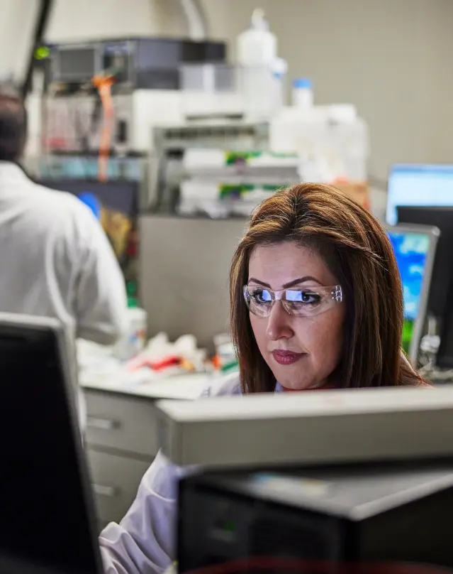 a person working at a computer in a lab with another person in the background