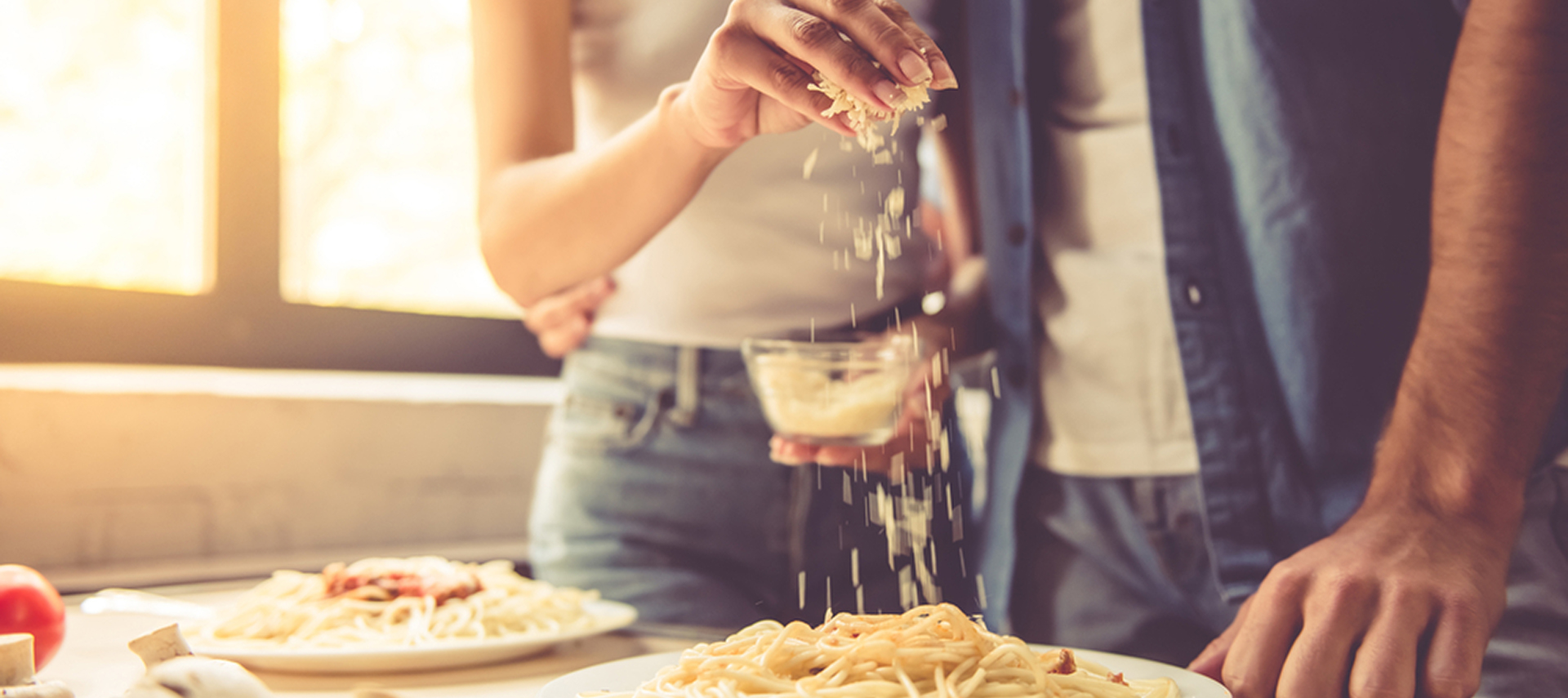 Cropped image of beautiful young couple eating spaghetti in kitchen at home. Woman is adding grated cheese