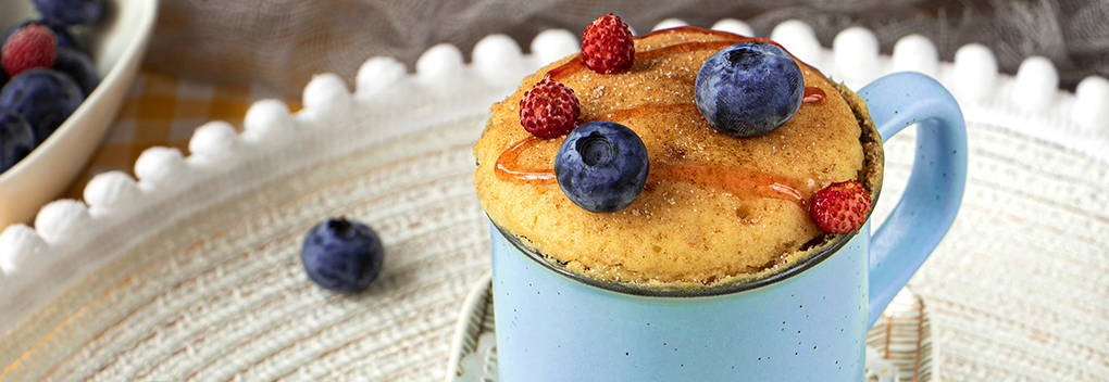 blueberry muffin in a mug, with blueberries, raspberries and honey drizzled on top