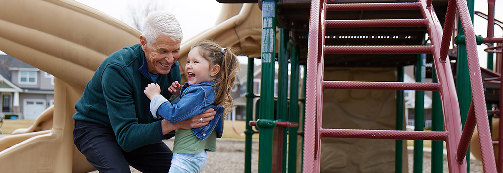 grandfather and granddaughter laugh and embrace while playing in the park