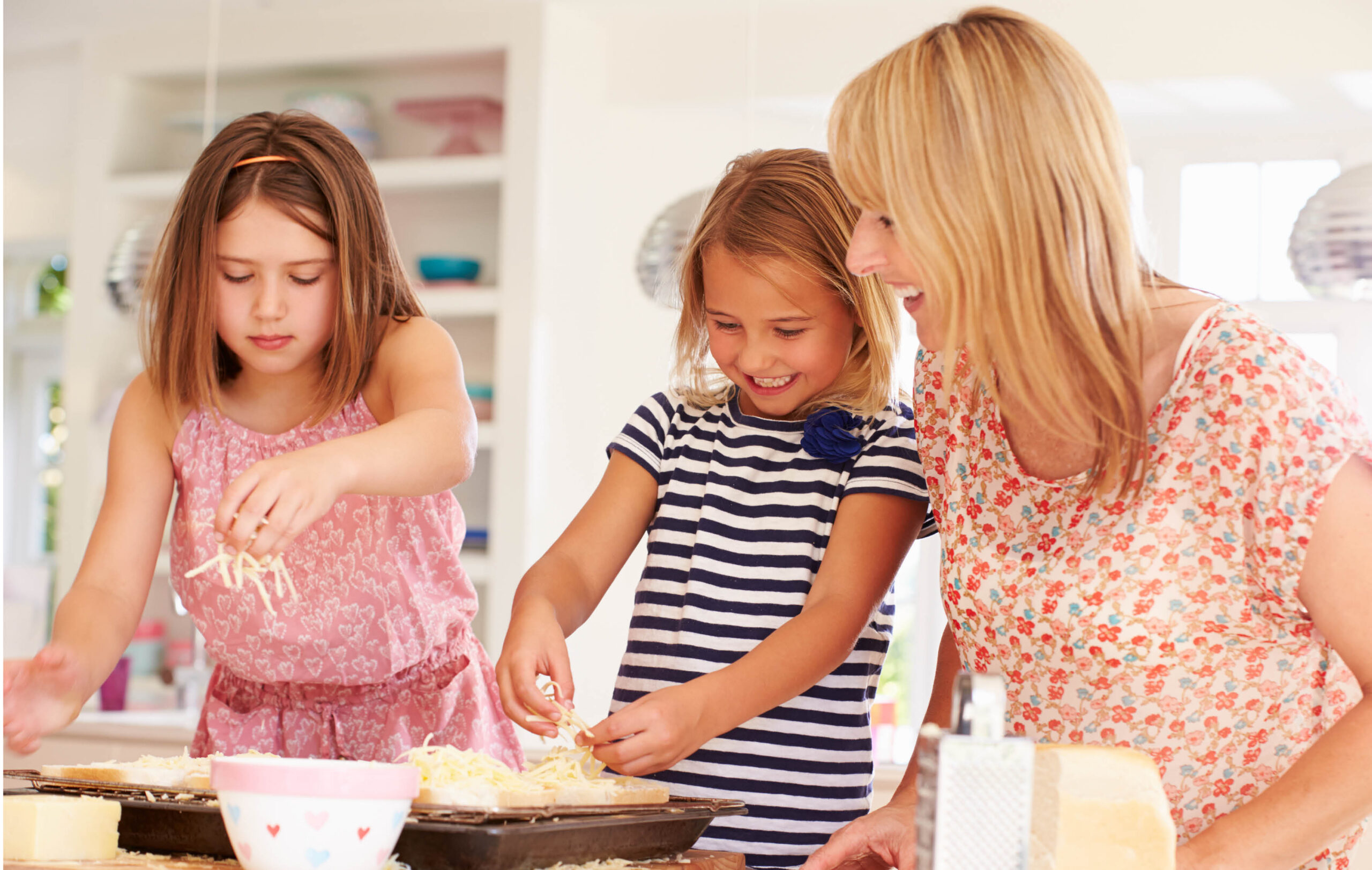 Mom and two school-aged daughters cooking with fresh shredded mozzarella cheese